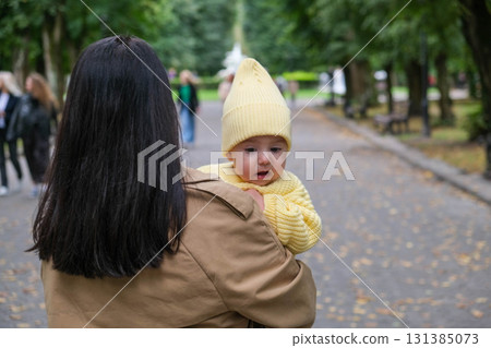 Mother Holding Baby in Yellow Outfit at Park 131385073