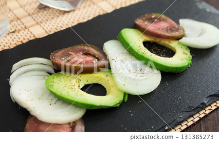 chopped vegetables black tomatoes, avocado and onions against black stone board 131385273