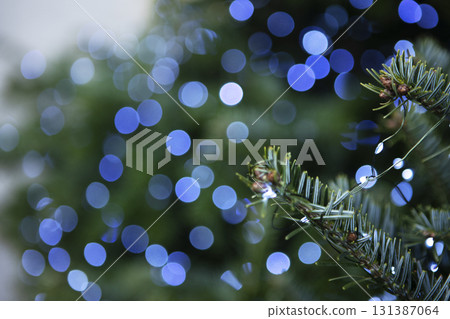 Blue lights of Christmas garland. Christmas garlands and fir branches. Christmas texture for postcards. Garland with lights on Christmas tree. 131387064