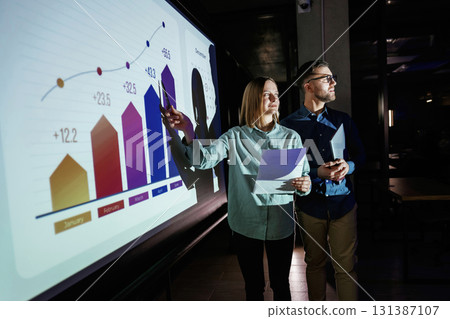 Man and woman are standing near projector with business data, cooperation Man and woman are standing near projector with business data, cooperation 131387107