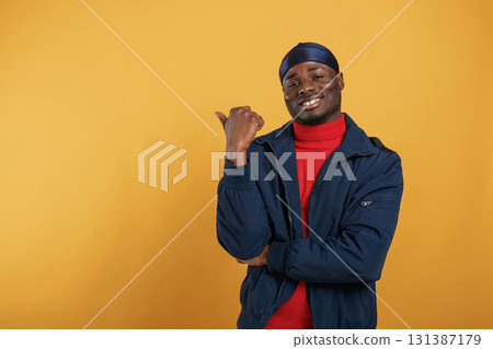 Showing something behind him by finger. Handsome black man is in the studio against yellow background 131387179