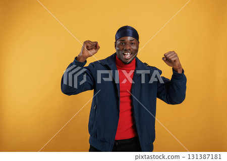 Having fun, celebrating success, hands up. Handsome black man is in the studio against yellow background 131387181