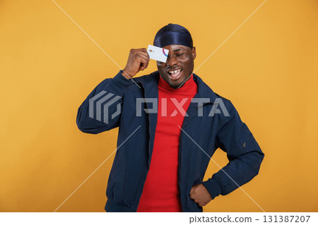 Covering eye by credit card. Handsome black man is in the studio against yellow background Covering eye by credit card. Handsome black man is in the studio against yellow background 131387207