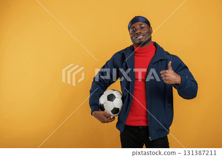Holding soccer ball. Handsome black man is in the studio against yellow background Holding soccer ball. Handsome black man is in the studio against yellow background 131387211