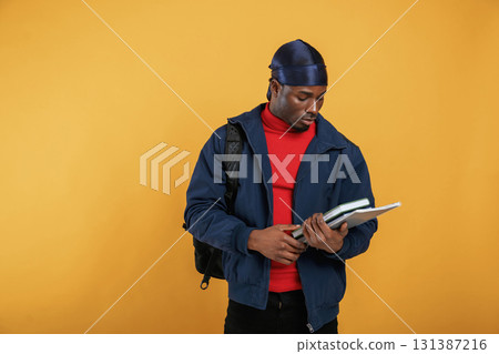 Student with books, backpack and notepad. Handsome black man is in the studio against yellow background Student with books, backpack and notepad. Handsome black man is in the studio against yellow background 131387216