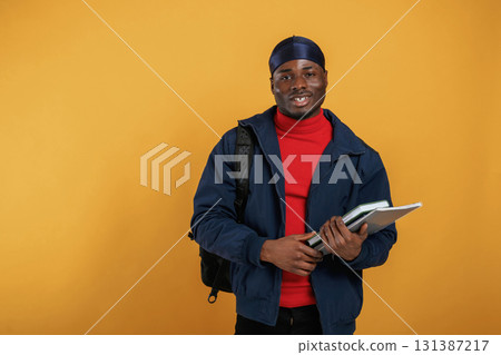 Student with books, backpack and notepad. Handsome black man is in the studio against yellow background Student with books, backpack and notepad. Handsome black man is in the studio against yellow background 131387217
