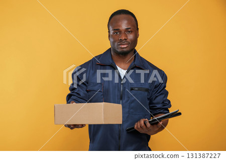 Delivery service worker with box. Handsome black man is in the studio against yellow background Delivery service worker with box. Handsome black man is in the studio against yellow background 131387227