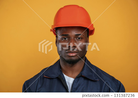 In orange hard hat. Construction worker. Handsome black man is in the studio against yellow background 131387236