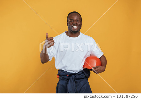 Holding hard hat in hand. Handsome black man is in the studio against yellow background 131387250
