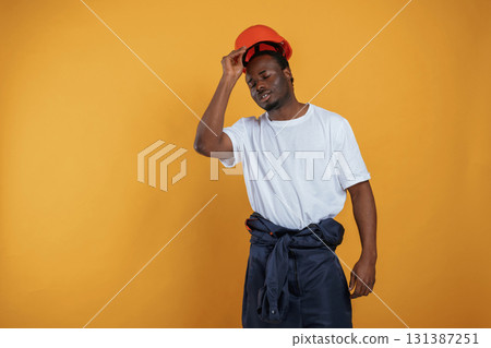 Wearing off the hard hat, construction worker. Handsome black man is in the studio against yellow background 131387251