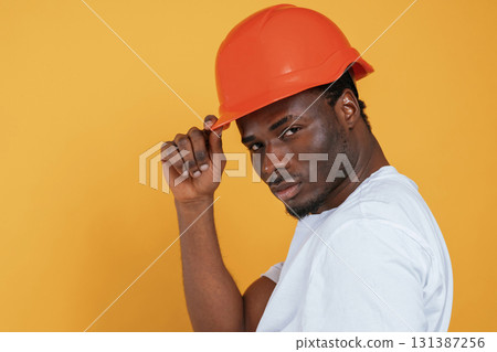 In orange hard hat. Construction worker. Handsome black man is in the studio against yellow background In orange hard hat. Construction worker. Handsome black man is in the studio against yellow background 131387256