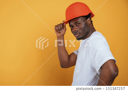 In orange hard hat. Construction worker. Handsome black man is in the studio against yellow background 131387257