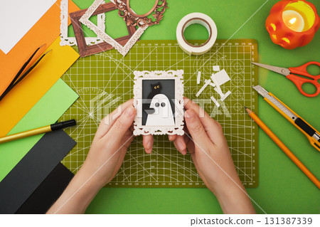 Making a Halloween decoration. Hands holding a small Halloween craft picture with a ghost and black cat 131387339