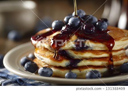 Blueberry pancakes are stacked high and covered with syrup and fresh berries. 131388409