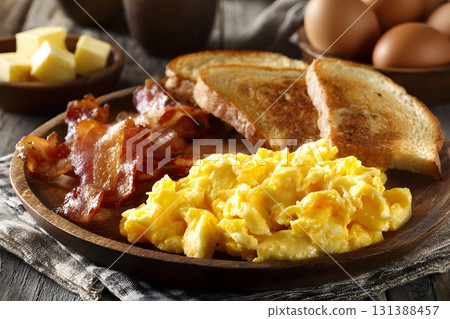 American breakfast plate with scrambled eggs, bacon, and toast on a wooden table. 131388457