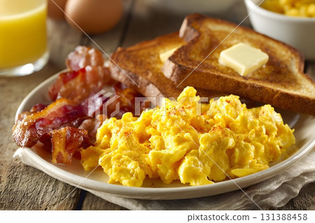 A plate of scrambled eggs with bacon and toast sits ready to eat. 131388458
