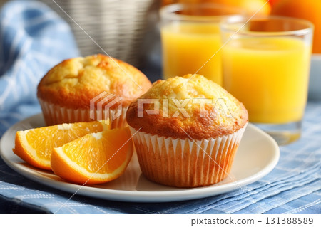 Golden muffins sit with bright orange slices beside refreshing orange juice. 131388589