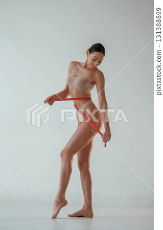 With measuring tape. Woman with slim body shape is posing against background With measuring tape. Woman with slim body shape is posing against background 131388899