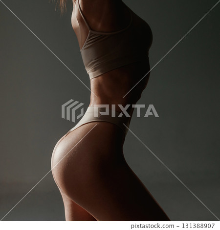In the sunlight, shadows. Woman with slim body shape is posing against background In the sunlight, shadows. Woman with slim body shape is posing against background 131388907