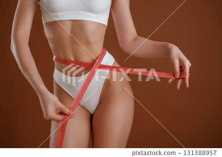 Dieting conception, with measuring tape. Woman with slim body shape is posing against background 131388957