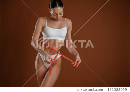 Dieting conception, with measuring tape. Woman with slim body shape is posing against background Dieting conception, with measuring tape. Woman with slim body shape is posing against background 131388959