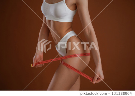 Measuring the leg, conception of weight loss. Woman with slim body shape is posing against background Measuring the leg, conception of weight loss. Woman with slim body shape is posing against background 131388964