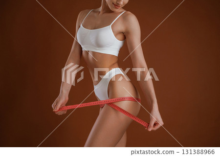 Measuring the leg, conception of weight loss. Woman with slim body shape is posing against background Measuring the leg, conception of weight loss. Woman with slim body shape is posing against background 131388966