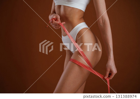 Tape over the leg, measuring, conception of diet. Woman with slim body shape is posing against background 131388974