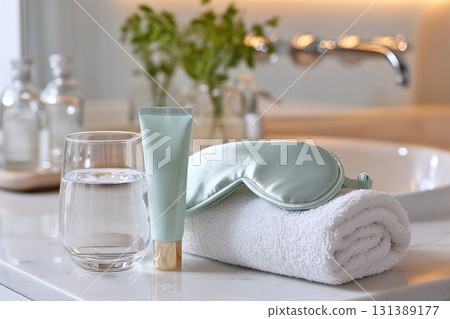 Relaxing sleep tourism setup with skincare products, water, and soft towel on marble countertop 131389177