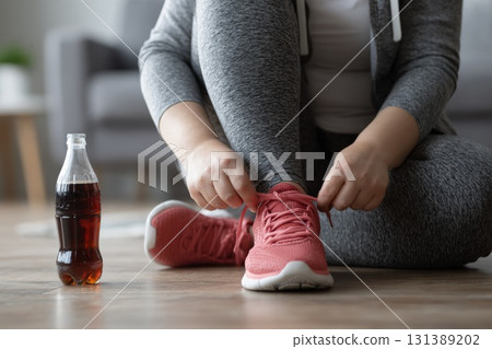 Sporty woman tying sneakers near soda bottle, concept of sugar and fitness contradiction 131389202