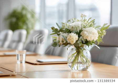 Elegant floral arrangement in glass vase on conference table with modern office decor elements Elegant floral arrangement in glass vase on conference table with modern office decor elements 131389334