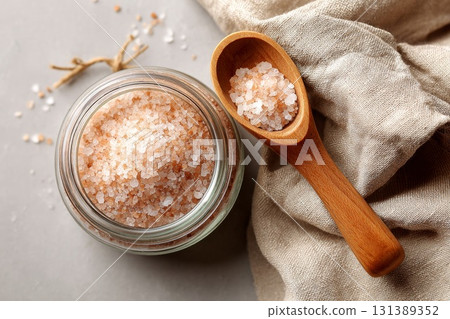 Glass jar filled with pink Himalayan salt beside wooden spoon on textured fabric surface Glass jar filled with pink Himalayan salt beside wooden spoon on textured fabric surface 131389352