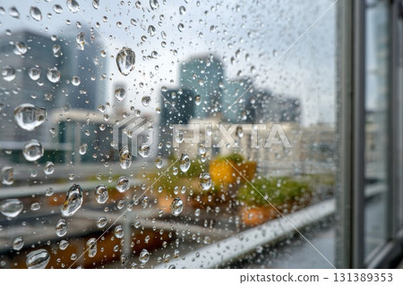 Close-up view of raindrops on glass with blurred cityscape background showcasing urban atmosphere 131389353