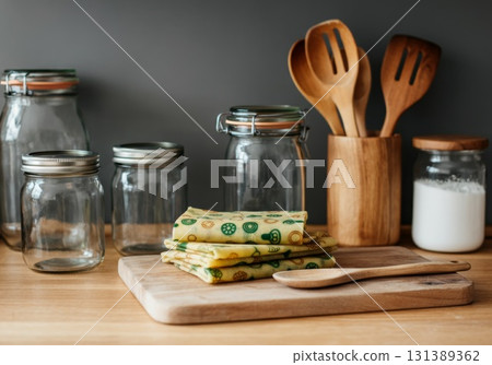 Reusable beeswax wraps stacked on wooden cutting board with kitchen utensils and jars 131389362