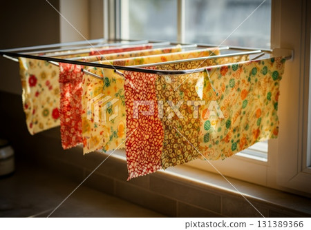 Colorful reusable beeswax wraps hanging on a drying rack near a sunlit window for eco-friendly storage 131389366