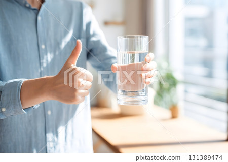 Glass of clear drinking water held up with a thumbs up gesture showing approval. 131389474