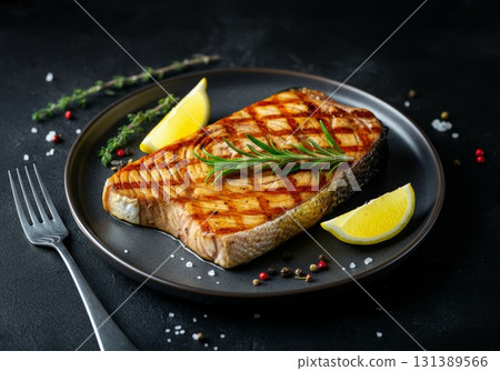 Grilled blue marlin swordfish steak garnished with lemon and herbs on a dark plate 131389566