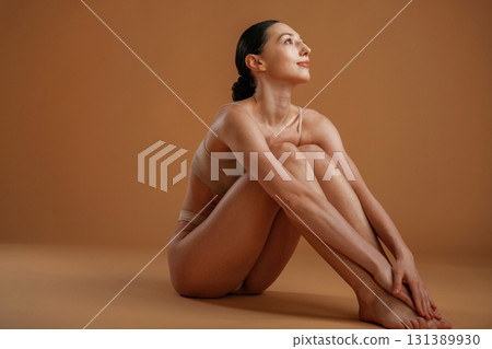 Sitting and resting on the floor. Woman with slim body shape is posing against background 131389930
