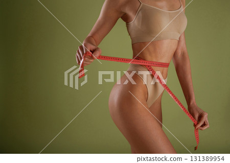 Results of diet, with measuring tape. Woman with slim body shape is posing against background 131389954