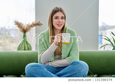 Portrait of relaxed beautiful young woman sitting at home on sofa with cup Portrait of relaxed beautiful young woman sitting at home on sofa with cup 131390374