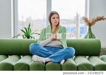 Portrait of relaxed beautiful young woman sitting at home on sofa with cup Portrait of relaxed beautiful young woman sitting at home on sofa with cup 131390375