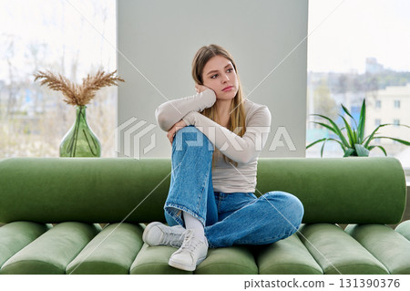 Unhappy upset young woman sitting on sofa at home, face close-up Unhappy upset young woman sitting on sofa at home, face close-up 131390376