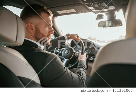 Driving, focused. Man in black suit is sitting in the car, driving Driving, focused. Man in black suit is sitting in the car, driving 131391003