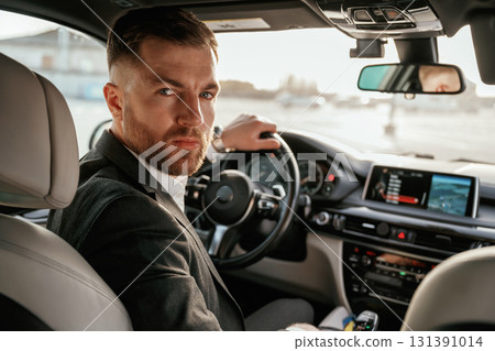 Looking behind at the camera. Man in black suit is sitting in the car, driving Looking behind at the camera. Man in black suit is sitting in the car, driving 131391014