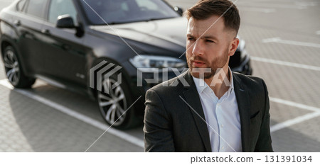 Businessman in suit is near his black car outdoors 131391034