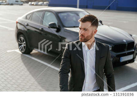 Businessman in suit is near his black car outdoors Businessman in suit is near his black car outdoors 131391036