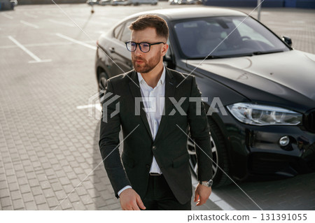 Handsome smart guy in glasses. Businessman in suit is near his black car outdoors 131391055