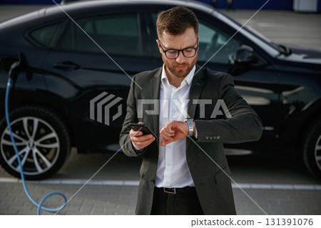 Handsome smart guy in glasses. Businessman in suit is near his black car outdoors Handsome smart guy in glasses. Businessman in suit is near his black car outdoors 131391076