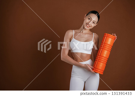 Orange colored fitness roll. Beautiful woman is in the studio 131391433