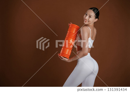 Orange colored fitness roll. Beautiful woman is in the studio 131391434
